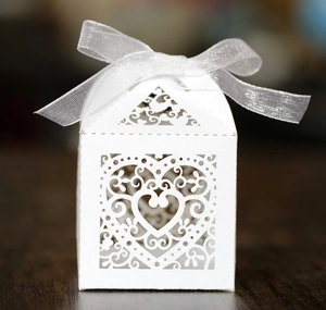 Close-up of laser-cut heart pattern on white wedding candy box with silk ribbon