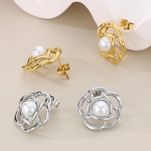 Detail of rose-shaped hollow metal earrings with a pearl center in gold and silver