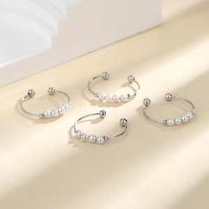 Silver twisted open ring with four movable white pearls on a minimalist background