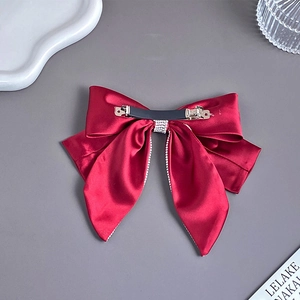 Detailed view of red satin bow hair clip featuring sparkling rhinestones and metal spring clip