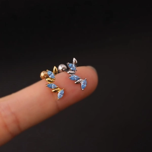 Macro shot of wing-shaped 16G ear studs with blue zircons in gold and silver finish