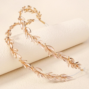 Detail of gold leaf vine bridal headband with white enamel accents on textured beige surface