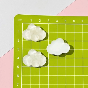 Detailed view of three cloud-shaped resin charms in white and translucent texture on a mat