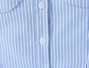 Detail of blue and white vertical striped fabric with neat stitching and white buttons