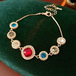Macro shot of gold bracelet with red square stone and multi-colored gems on green velvet