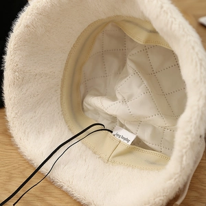 Detail of white plush bucket hat featuring quilted interior lining and adjustable drawstring
