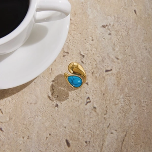 Detail of a gold titanium ring with a teardrop turquoise stone on a stone surface