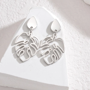 Detail of silver monstera leaf earrings on a minimalist white stone pedestal background