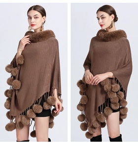 Detailed view of brown knitted poncho featuring a plush faux fur collar and decorative pom-poms