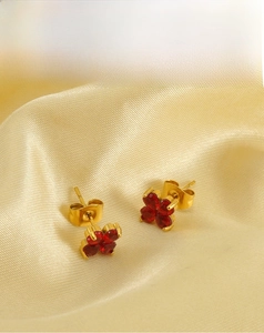 Détail de boucles d'oreilles trèfle avec cristaux rouges et base en acier doré
