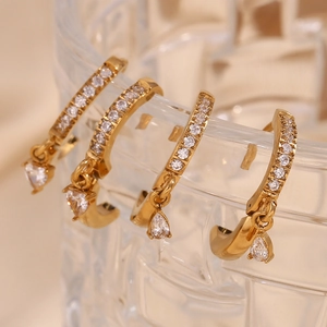 Detail of four 18K gold plated hoop earrings with zircon heart and drop charms on glass