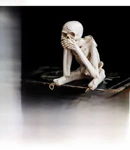 Détail d'une statuette de crâne en résine dans la position de ne rien entendre sur livres
