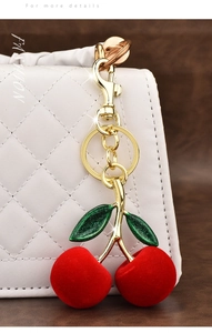 Detailed close-up of red velvet cherry keychain on a white quilted shoulder bag
