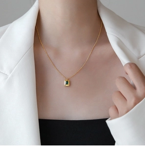 Detail of a square green gemstone pendant on a gold bead chain worn with a white blazer