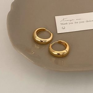 Detailed view of chunky gold hoop earrings with polished finish on a ceramic plate