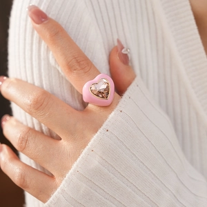 Close-up of pink heart-shaped enamel ring featuring a large pink heart gemstone on finger