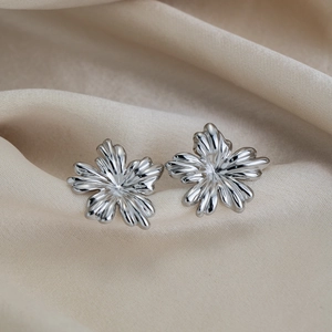 Macro shot of silver floral earrings with detailed petal texture on beige silk fabric