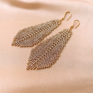 Detail of golden rhinestone feather leaf drop earrings on champagne silk background