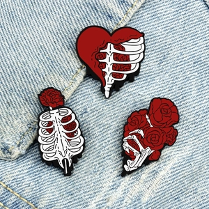 Three skeleton and red rose enamel pins displayed on blue denim fabric background
