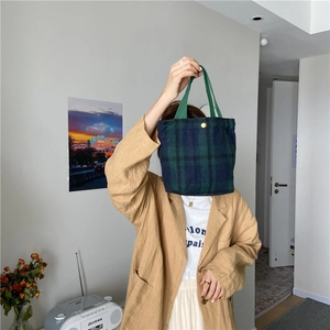 Detail of green and navy tartan fabric tote with golden metal clasp and woven handle