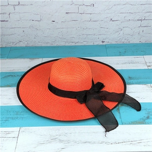 Detail of orange woven straw sun hat featuring a black mesh bow ribbon for summer beach trips