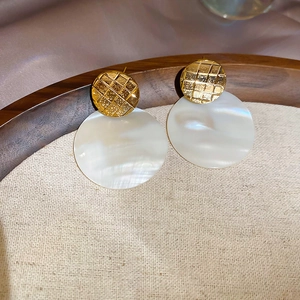 Dettaglio di orecchini placcati oro 24k con madreperla e zircone su tessuto di seta
