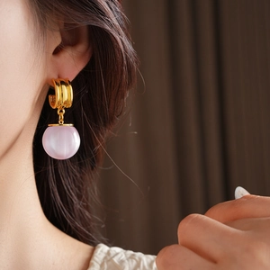 Detail showing the pink cat-eye stone drop earring on a model with elegant gold metal ring