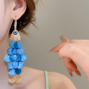 Detailed view of long gold fish-shaped earrings with blue shell scales on a model