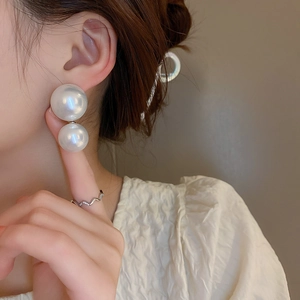 Close-up of elegant double large faux pearl drop earrings on a model with warm lighting