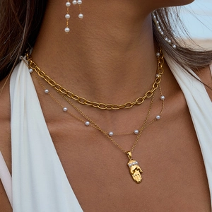 Ensemble de colliers superposés plaqués or 18k avec perles et pendentif main sur un mannequin