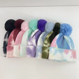 Detail of multi-color tie-dye knit beanies with large matching faux fur pom-poms