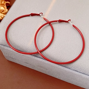 Detail view of large red circular hoop earrings on a textured brown leather background