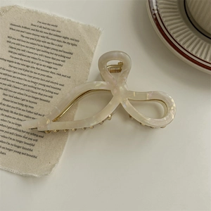 Detail of pearlescent white bow hair claw clip showing internal metal spring and teeth