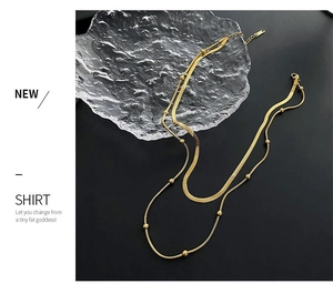 Detail of gold double-layer necklace featuring snake chain and bead chain on glass plate