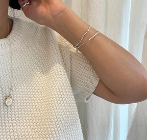 Detail of silver twisted chain bracelet and coin pendant necklace on knitted fabric