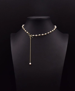 Detail of elegant gold bow pendant with white pearls and long tassel on a black display