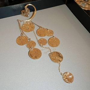 Dettaglio di ear cuff a cuore dorato con trama martellata e nappe di paillettes