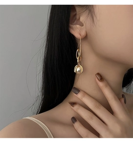 Detailaufnahme langer goldener Perlenohrringe im minimalistischen Design an einem Model