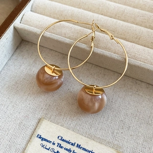 Detail of gold hoop earrings with brown resin beads on a beige velvet jewelry box tray