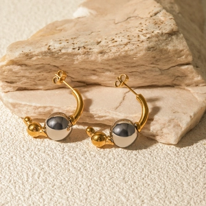 Detail of two-tone C-shaped hoop earrings with gold and silver beads on a stone background