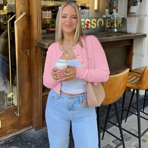 Gros plan du cardigan en maille rose avec boutons dorés dans un café en plein air