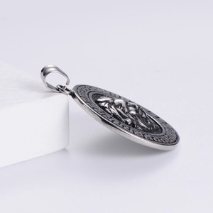 Detail of round lion head pendant with Greek fret pattern border on a white prop