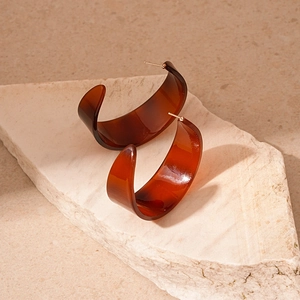 Macro detail of amber tortoiseshell C-shaped acrylic earrings on beige stone background