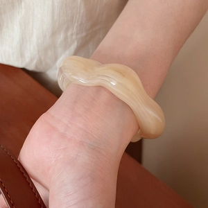 Detail shot of wavy acrylic bangle with cream marble texture worn on wrist