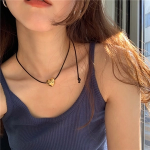 Polished gold heart pendant on minimalist black cord necklace worn by model