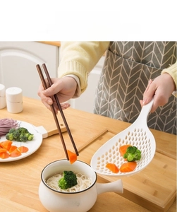 Macro detail of large white nylon slotted spoon with long handle and wooden chopsticks
