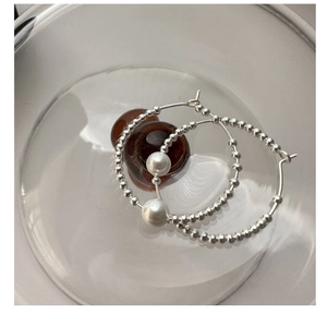 Detail of silver beaded hoop earrings with white pearl displayed in a glass bowl