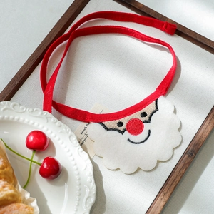 Detail of Christmas Santa embroidered dog bib with red ribbons on a lifestyle tray
