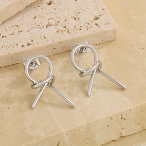 Macro detail of silver knot-shaped earrings on textured light beige travertine stone