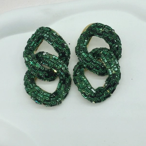 Macro view of emerald green rhinestone pavé on interlocking golden chain earrings